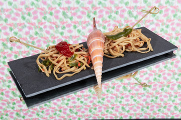 Photo detail of Italian pasta served on a black stone plate next to a seashell, with a colorful background. Concept of healthy food.