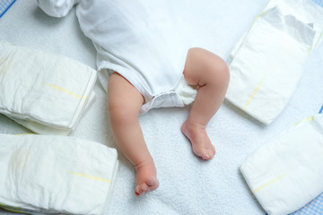 Feet of newborn baby on changing table with diapers. Cute little girl or boy two weeks old. Dry and healthy body and skin concept. Baby nursery.