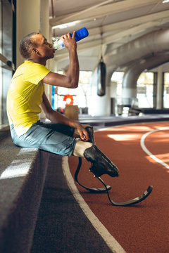 Athlete with prosthetic legs drinking water by running track
