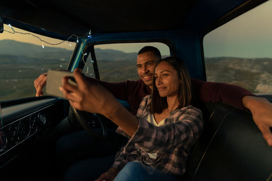 Young couple on a road trip taking a selfie in their car at dusk