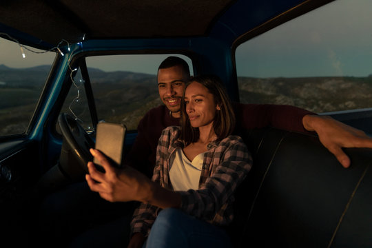 Young couple on a road trip taking a selfie in their car at dusk