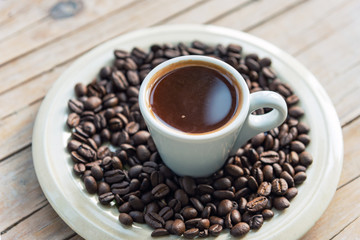 Hot Espresso in white cup and roasted coffee beans on a wooden table, close up