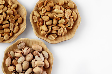 wood plates of salted peanuts and pistachios on white background. snack to beer