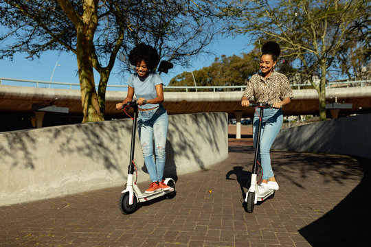 Two young women riding e scooters - Powered by Adobe