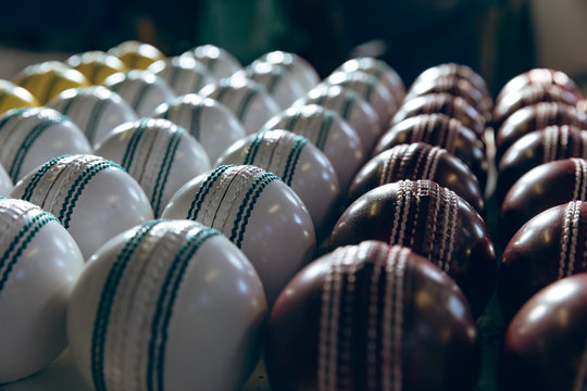 Red, white and yellow cricket balls in rows