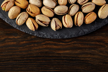 top view of salted pistachio nuts on stone board on wood background. copy space