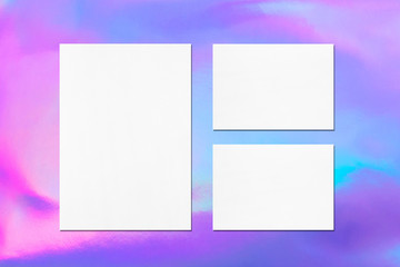 One empty white vertical a4 sized poster and two a5 sized horizontal rectangle card mockups with soft shadows on holographic background. Flat lay, top view