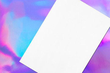 Close up of empty white rectangle poster mockup lying diagonally with soft shadow on holographic background. Flat lay, top view. Open composition.