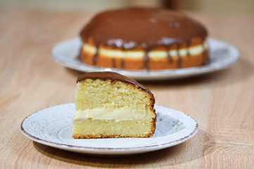 Piece of Boston cream pie in front with the whole pie in the background.
