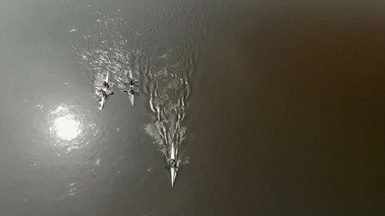 Three kayaks floating on the river, leaving behind a wave in the water reflects the sun. Top view of the drone
