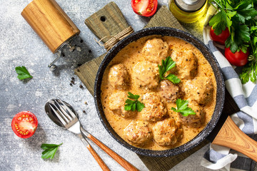 Meatballs in sour cream and tomato sauce in a frying pan on stone table. Top view flat lay.