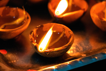 Macro shots of diyas being lit by hand or candle for the hindu religious festival of Diwali. These colorful earthern pots hold oil and a cotton wick to light