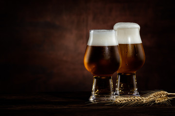 two glasses of cold dark beer and wheat spikelets on dark background. copy space