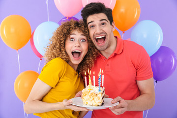 Image of positive couple man and woman celebrating birthday with multicolored air balloons and piece of cake