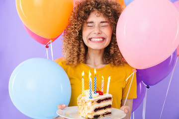 Image of joyful young woman celebrating birthday with multicolored air balloons and piece of cake