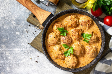 Meatballs in sour cream and tomato sauce in a frying pan on stone table. Top view flat lay. Free space for your text.