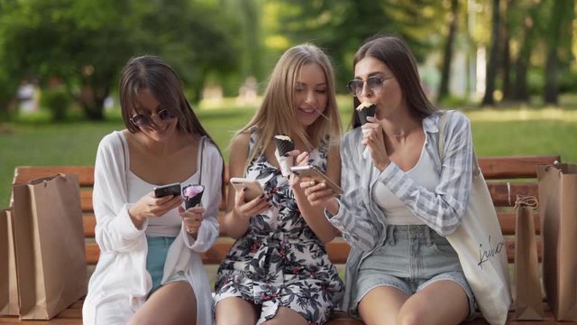 Three attractive girls together eating ice cream cones on a park bench