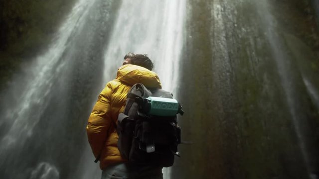 Young hiker in front of a waterfall looks around in a cave