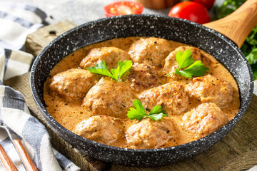 Meatballs in sour cream and tomato sauce in a frying pan on stone table.