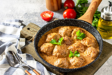 Meatballs in sour cream and tomato sauce in a frying pan on stone table. Free space for your text.