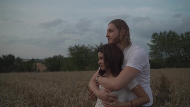 Medium cinematic handheld shot of a romantic mixed race couple standing in the middle of a hay wheat spike field holding each other passionately looking in the same direction grabing on breast