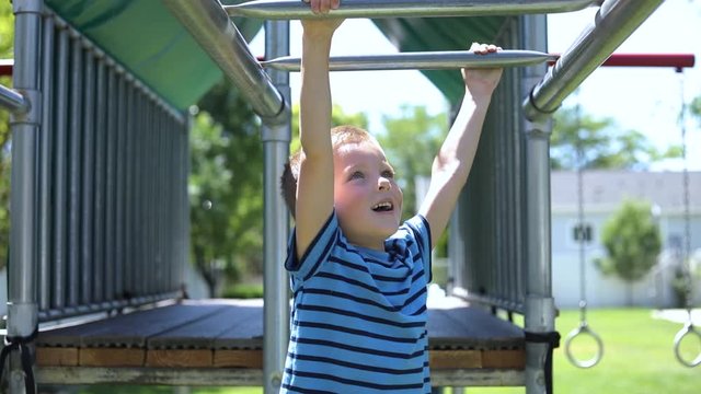 Slow Motion shot of a young boy playing on the monkey bars on a playground set in his backyard.