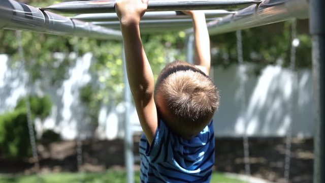 Slow Motion shot of a young boy playing on the monkey bars on a playground set in his backyard.