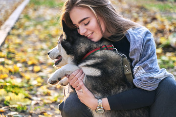 Obraz premium Young beautiful girl playing with her cute husky dog pet in autumn park covered with red and yellow fallen leaves