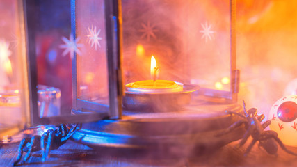 Halloween concept, spooky decorations with lighting up candle and candle holder with blue tone smoke around on a dark wooden table, close up.
