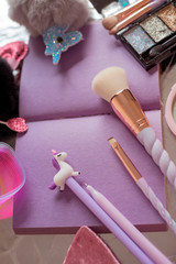 Purple pages notepad, fluffy ball toy, unicorn pen, sparkle eyeshadow palette, cosmetic brushes with twisted handles, rainbow highlighter and slinky