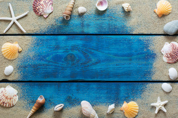 Summer border with various seashells, starfish and sand on blue wooden backround