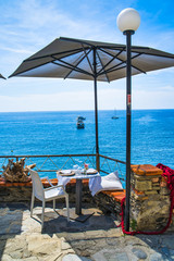 Monterosso al Mare, Italy - August 17, 2019: table under a parasol in a cafe on the mountain / sea view with boats and yachts / Cinque Terre