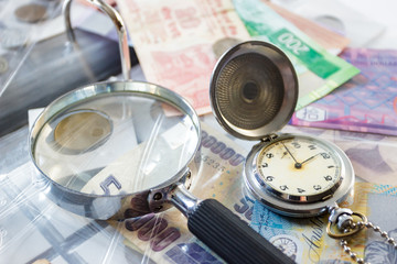 Different old collector's coins with a pocket watch, blurred background