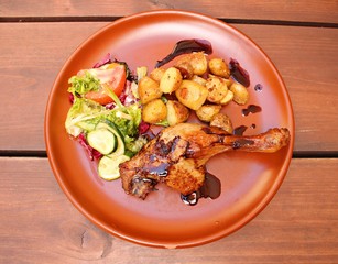 Grilled duck leg with potatoes and fresh salad on a ceramic plate