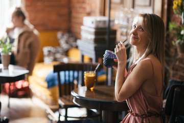 beautiful pensive calm relaxed girl blonde sits at a table in a retro vintage style cafe with a mug of drink and looks to the side