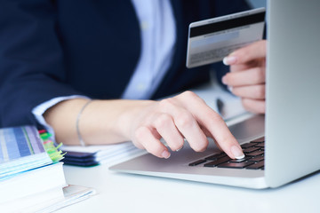 Businesswoman inputting her password and login to carry out online banking operation on laptop pc in the office. Woman's hand holding credit card close-up.