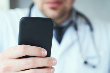 Male doctor hands with mobile phone close-up. Male doctor in white coat is using a modern smartphone device with touch screen.