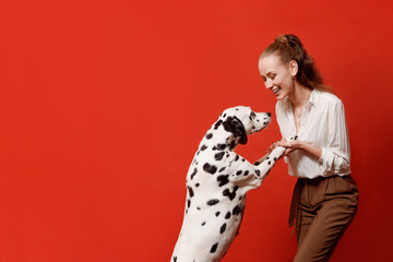 Side view, half face, profile portrait of attractive, pretty, charming woman raises dalmatian dog in front of face, blowing kiss to pet, isolated on red background. Copy space © Iulia