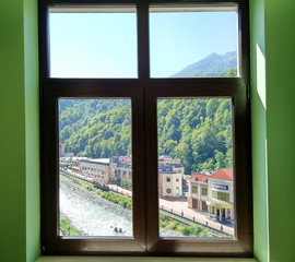 Obraz na płótnie Canvas Hotel window on ski resort in summer season - view of neighboring hotels, mountain river and mountains
