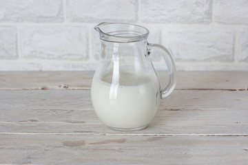 Dishes. Glass jug with milk on a white wooden table