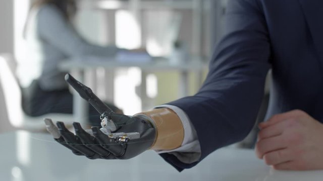 Close up shot of unrecognizable businessman holding holographic globe projected in the air with bionic prosthetic hand while sitting at desk in the office