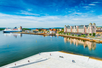 Fototapeta na wymiar Panorama of Oslo with historical buildings, port, cruise ship, promenade with walking people and the blue sky