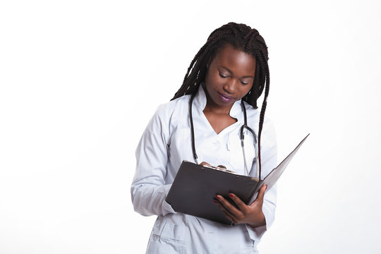 Female american african doctor, nurse woman wearing medical coat with stethoscope write good test results in hospital sheet chart. Happy excited for success medical worker posing on light background