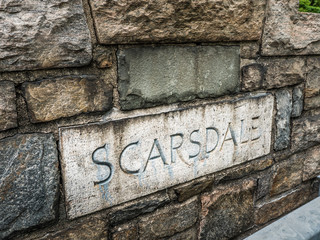 A sign reading Scarsdale with letters engraved in limestone in a stone wall along a stair leading...
