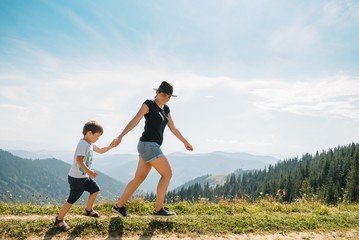 Smiling female hugs her son resting as they walking in mountains together