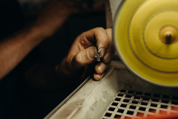 Crafting. Hands of the jeweler polishes silver jewelry brooch on the polishing wheel. Little gain...