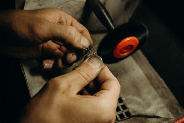 Crafting. Hands of the jeweler polishes silver jewelry brooch on the polishing wheel. Little gain on photo