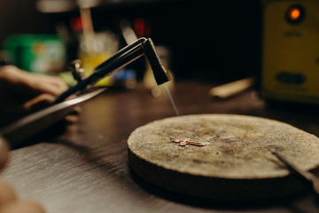 Crafting. Professional jeweler using gas torch for melting precious cross. Jewelry specialist directing the flame right on the sterling silver Little gain on photo