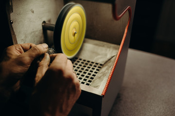 Crafting. Hands of the jeweler polishes silver jewelry brooch on the polishing wheel. Little gain on photo