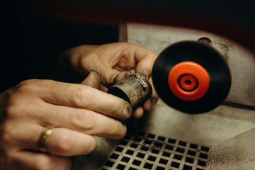 Crafting. Hands of the jeweler polishes silver jewelry brooch on the polishing wheel. Little gain on photo